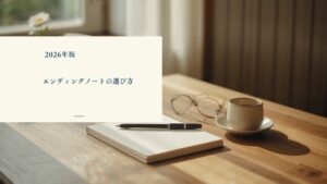 窓辺の木のテーブルに置かれたノートと万年筆・老眼鏡・湯のみ・白い花。エンディングノートのおすすめと選び方の記事アイキャッチ