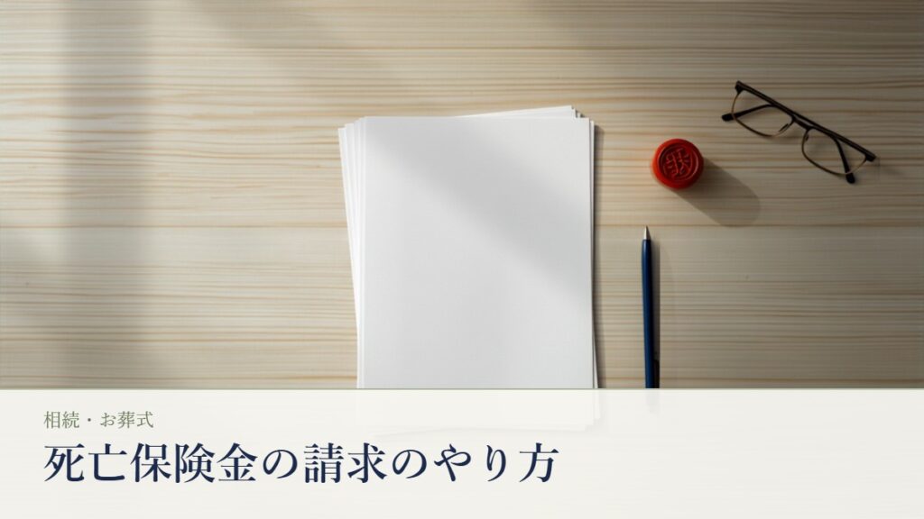 死亡保険金の請求書類とA4の申請用紙、朱肉と印鑑、ボールペンが並ぶ木の机の静物