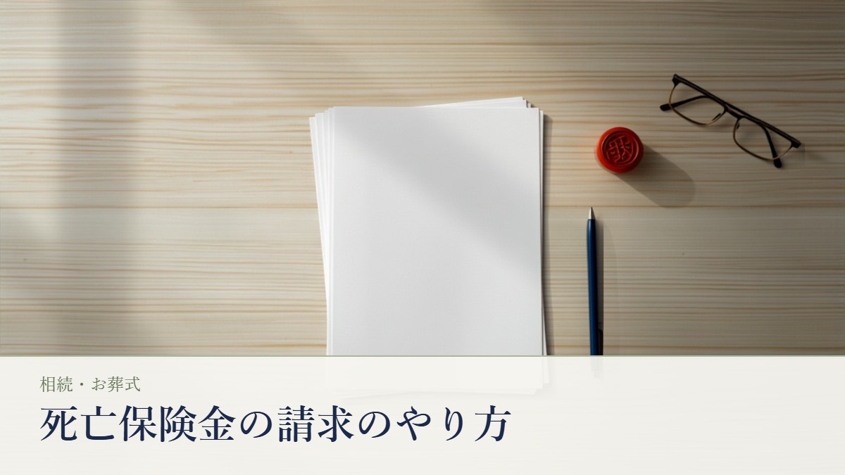死亡保険金の請求書類とA4の申請用紙、朱肉と印鑑、ボールペンが並ぶ木の机の静物