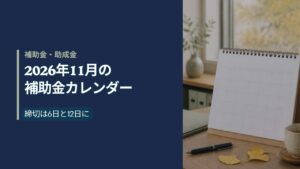 秋の窓辺の机に置かれた無地の卓上カレンダーと書類フォルダ（2026年11月の補助金カレンダー）
